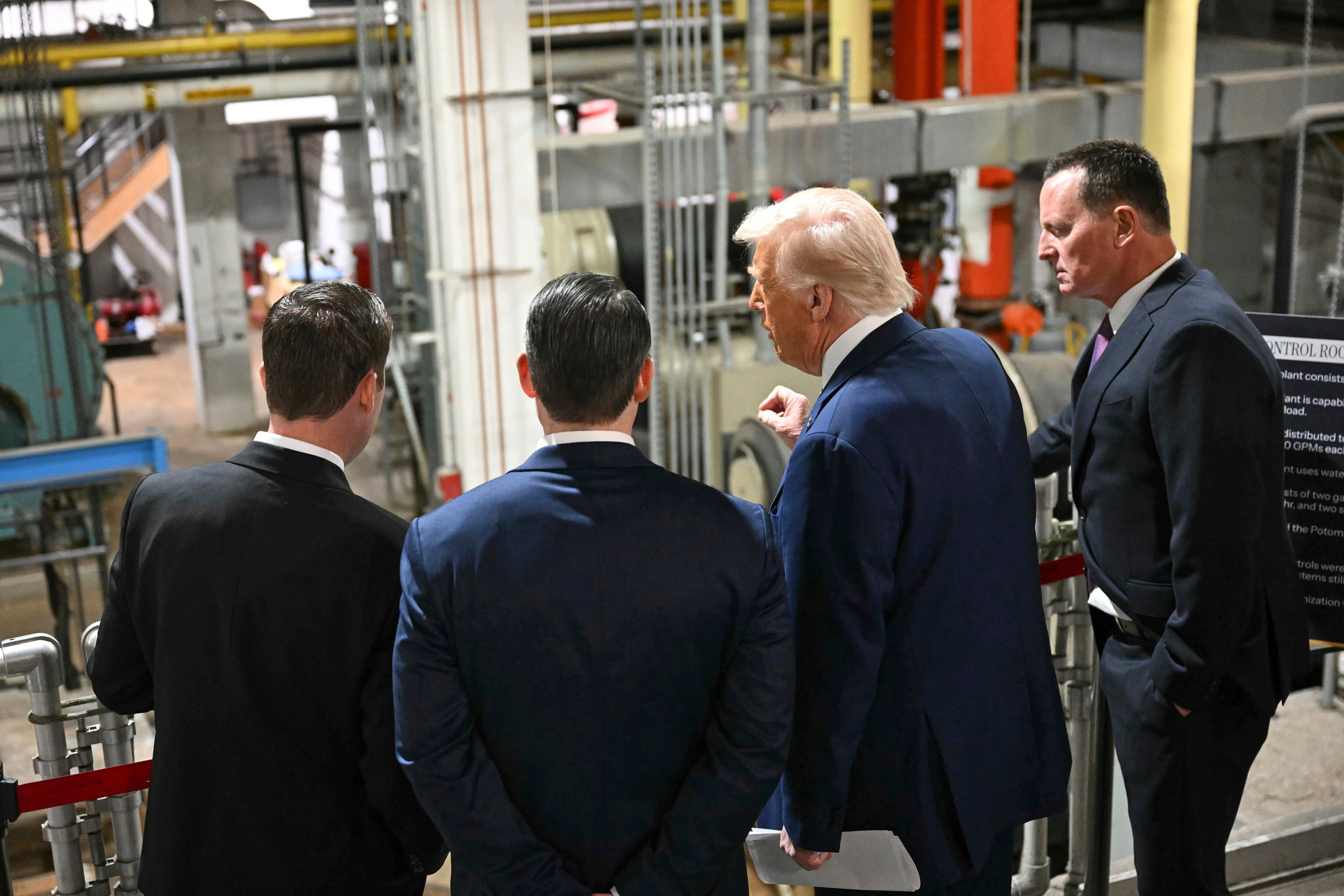 Donald Trump stands facing away from the camera with two men to his left and one man to his right