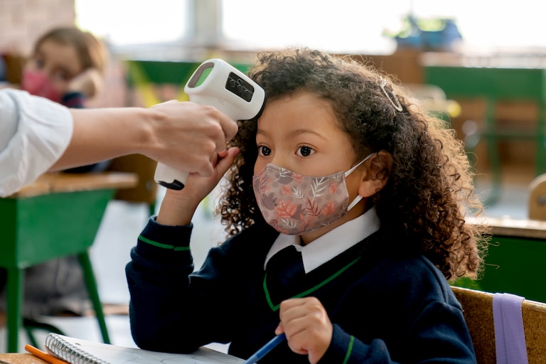 Latin American teacher checking the temperature of a girl at school using an infrared thermometer during the COVID-19 pandemic
