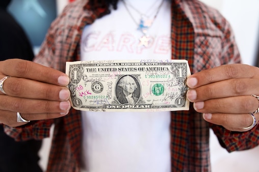SATURDAY, APRIL 11, 2026 - Carpet Company co-owner Ayman Abdeldayem holds up a dollar bill signed by a handful of the first people in line to enter the flagship story on its opening day.
