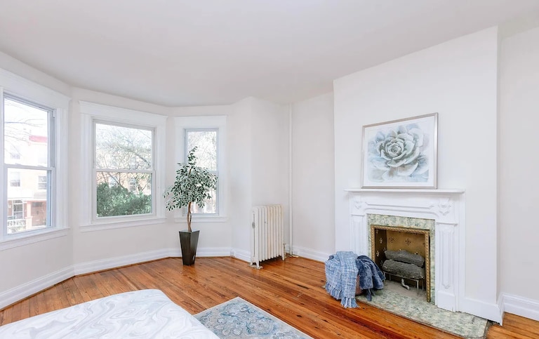 A second-floor bedroom with white walls, a fireplace and three windows that look out to the street.