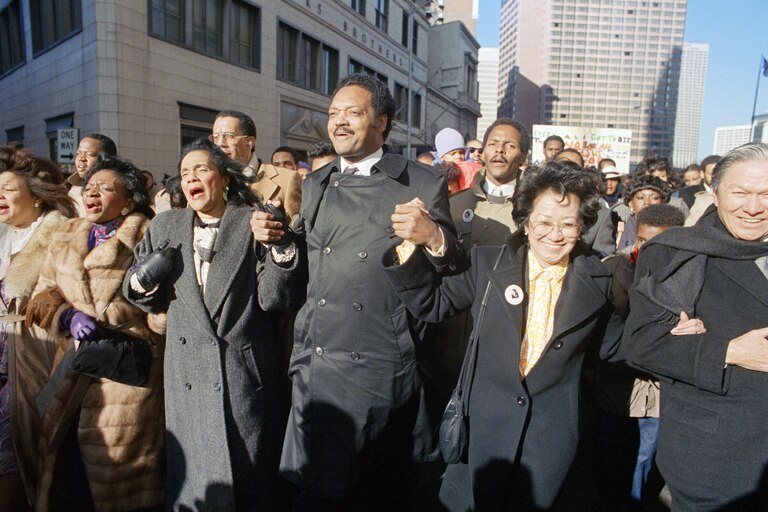 Coretta Scott King holds hands while singing with the Rev. Jesse Jackson and Christine Farris, the sister of Dr. Martin Luther King, Jr., as they parade on Peachtree Street in Atlanta on Monday, Jan. 19, 1987 to honor King's birthday.