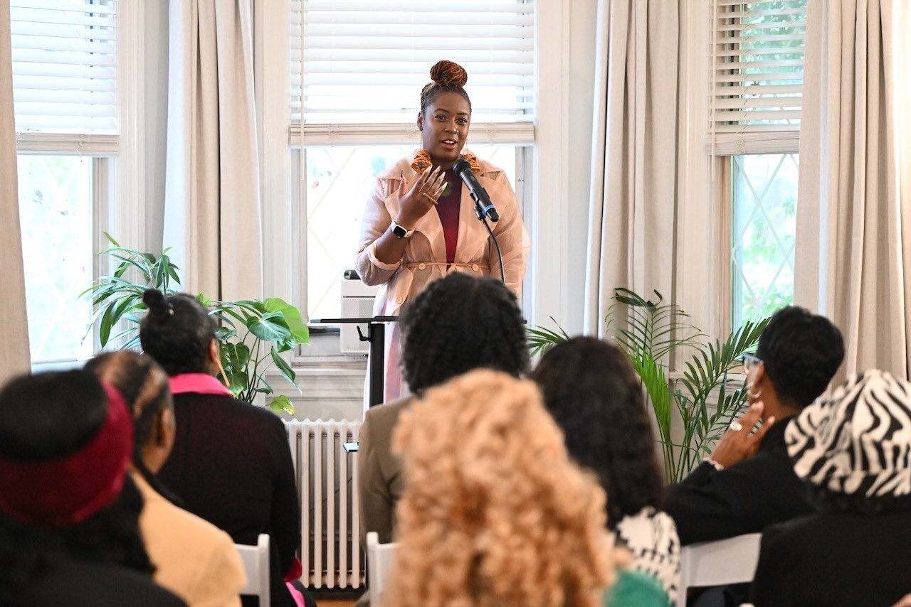 Lady Brion speaks at a podium to a room full of people.
