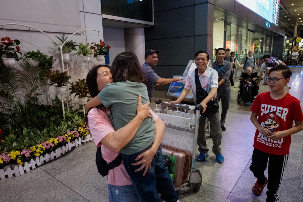 Ho Chi Minh, Vietnam - July 27, 2026: Melissa Tran, 44, hugs her daughter, Riley, 8, while her husband, Danny, 56, and her son, Jacob, 11, watch at the arrivals area at Tan Son Nhat International Airport in Ho Chi Minh, Vietnam on July 27, 2026. Rosem Morton for The Baltimore Banner
