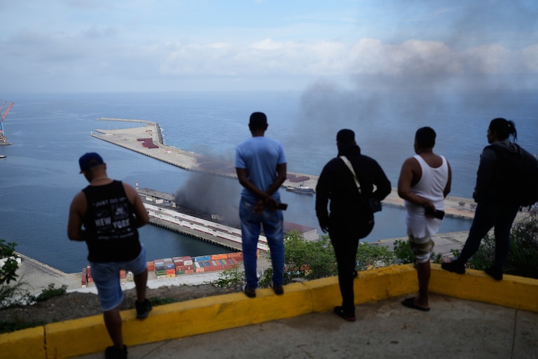 Men watch smoke rising from a dock after explosions were heard at La Guaira port, Venezuela, Saturday, Jan. 3, 2026.