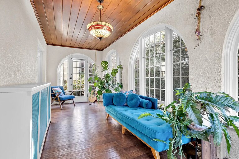 A bright sunroom with arched windows, dark wooden floors, a wood-stained ceiling and bright blue furniture.