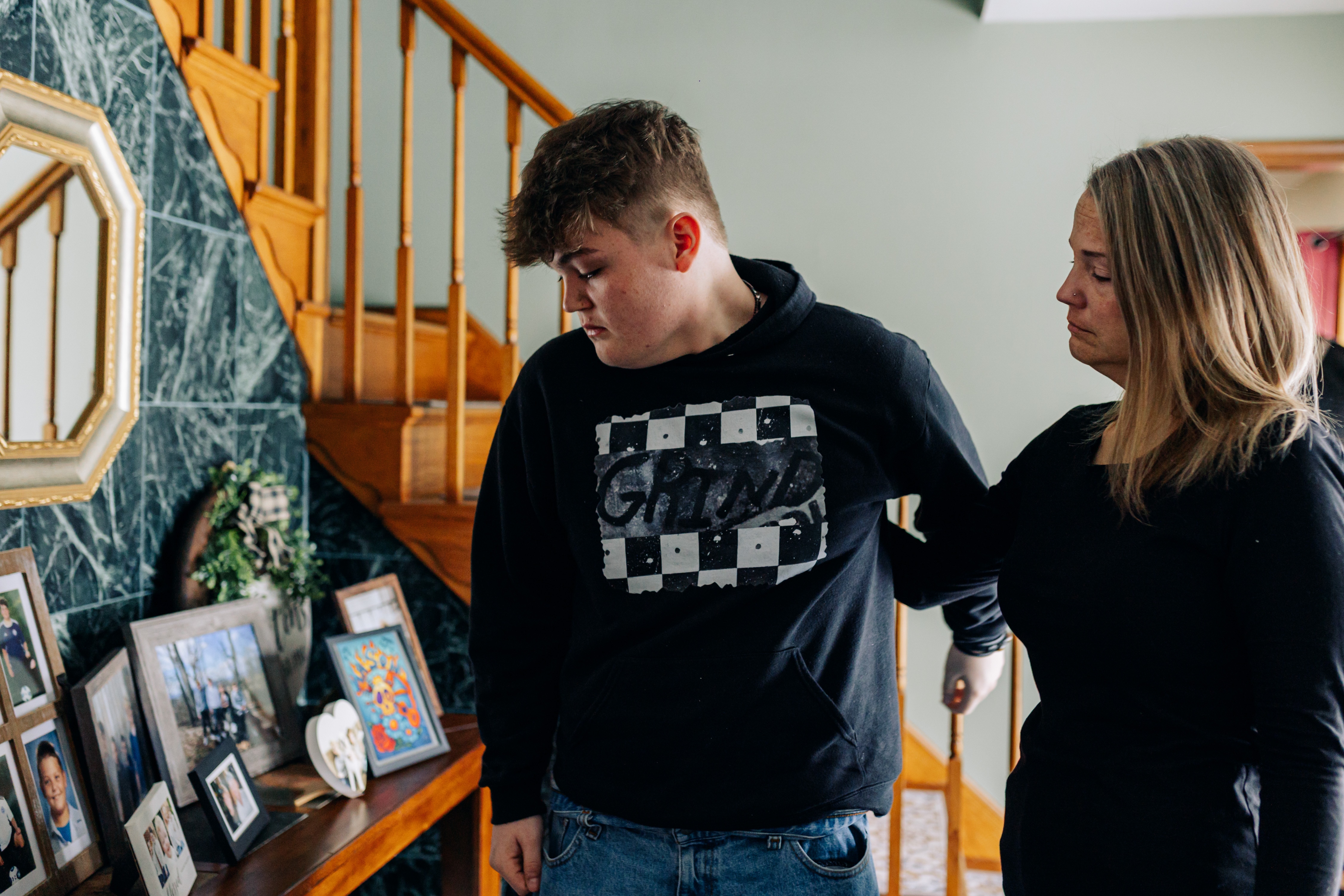 Erica Kearns and her son, Clay, 15, look at a table of family photos including Clay’s younger brother, Mason, who died at 13 after becoming trapped in a storm drain during flash flooding in July, at Erica’s parents’ house, in Mt. Airy, MD on Monday, Feb. 16, 2026.