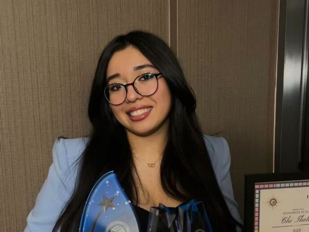 Andrea Rodriguez Avila wearing glasses and a powder blue suit jacket while holding an award.