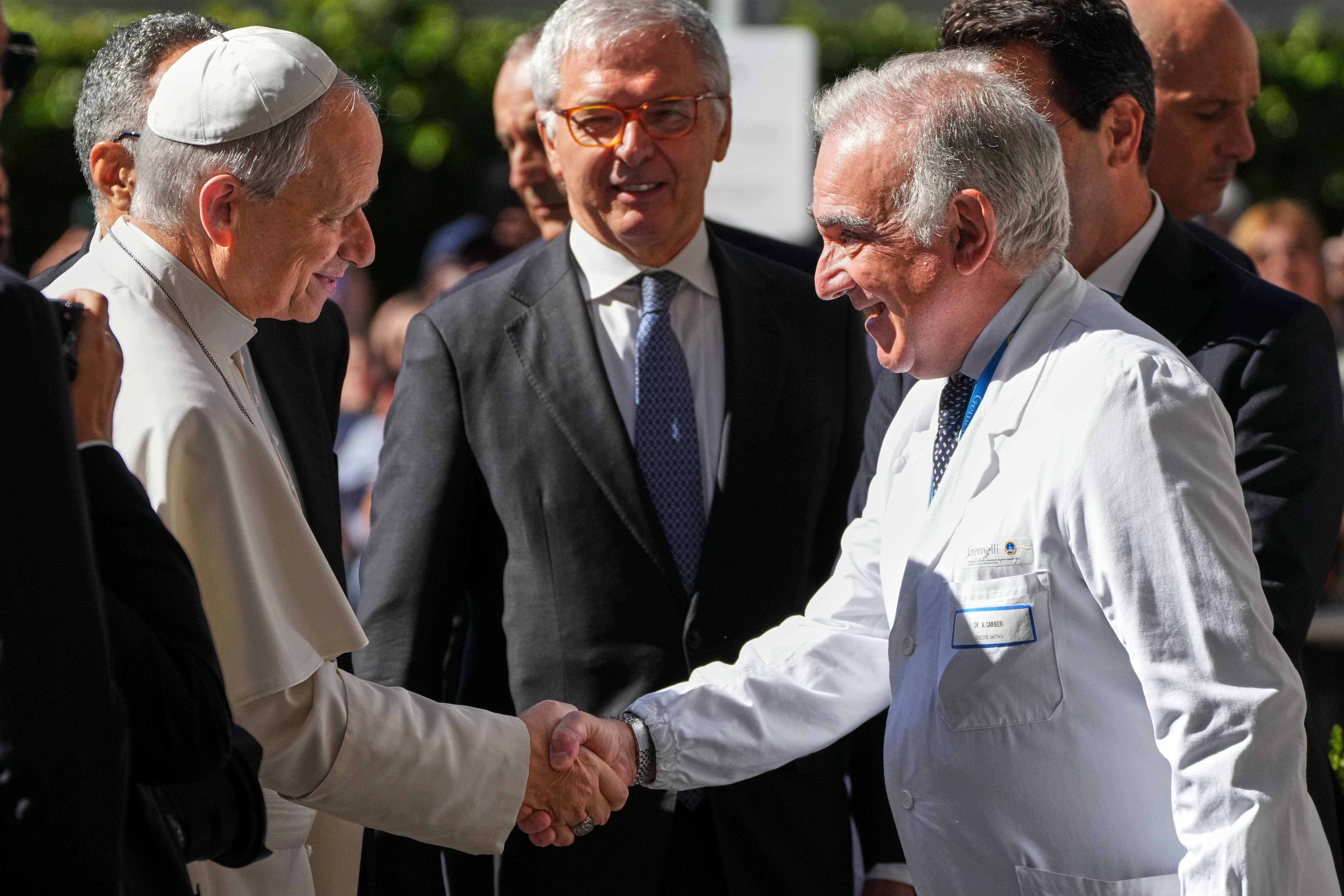 Pope Leo XIV shakes hands with Medical Director Andrea Cambieri, who wears a white coat, upon arriving at the Agostino Gemelli Polyclinic in Rome. Several men look on.