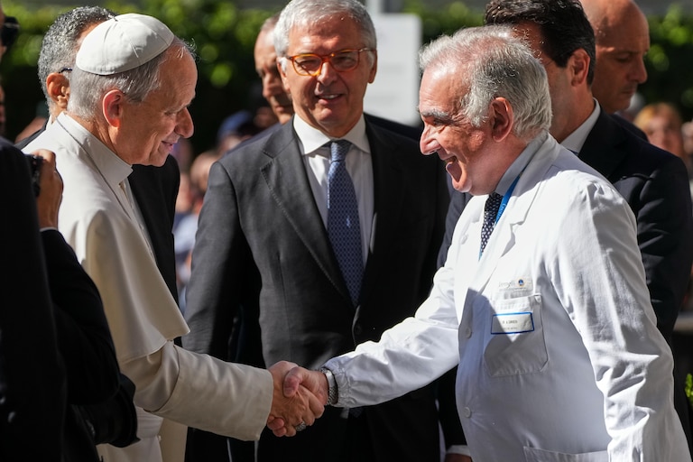Pope Leo XIV shakes hands with Medical Director Andrea Cambieri, who wears a white coat, upon arriving at the Agostino Gemelli Polyclinic in Rome. Several men look on.