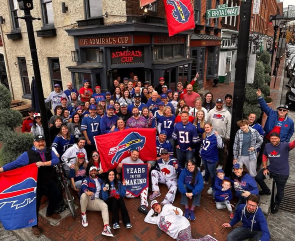 Several dozen members of the Baltimore Bills Backers pose outside of Fells Point bar The Admiral's Cup wearing Buffalo Bills jerseys and gear and carrying Bills flags and signs. The fan group started watching games on the upper levels of the bar and has flourished in recent years with the franchise's success.