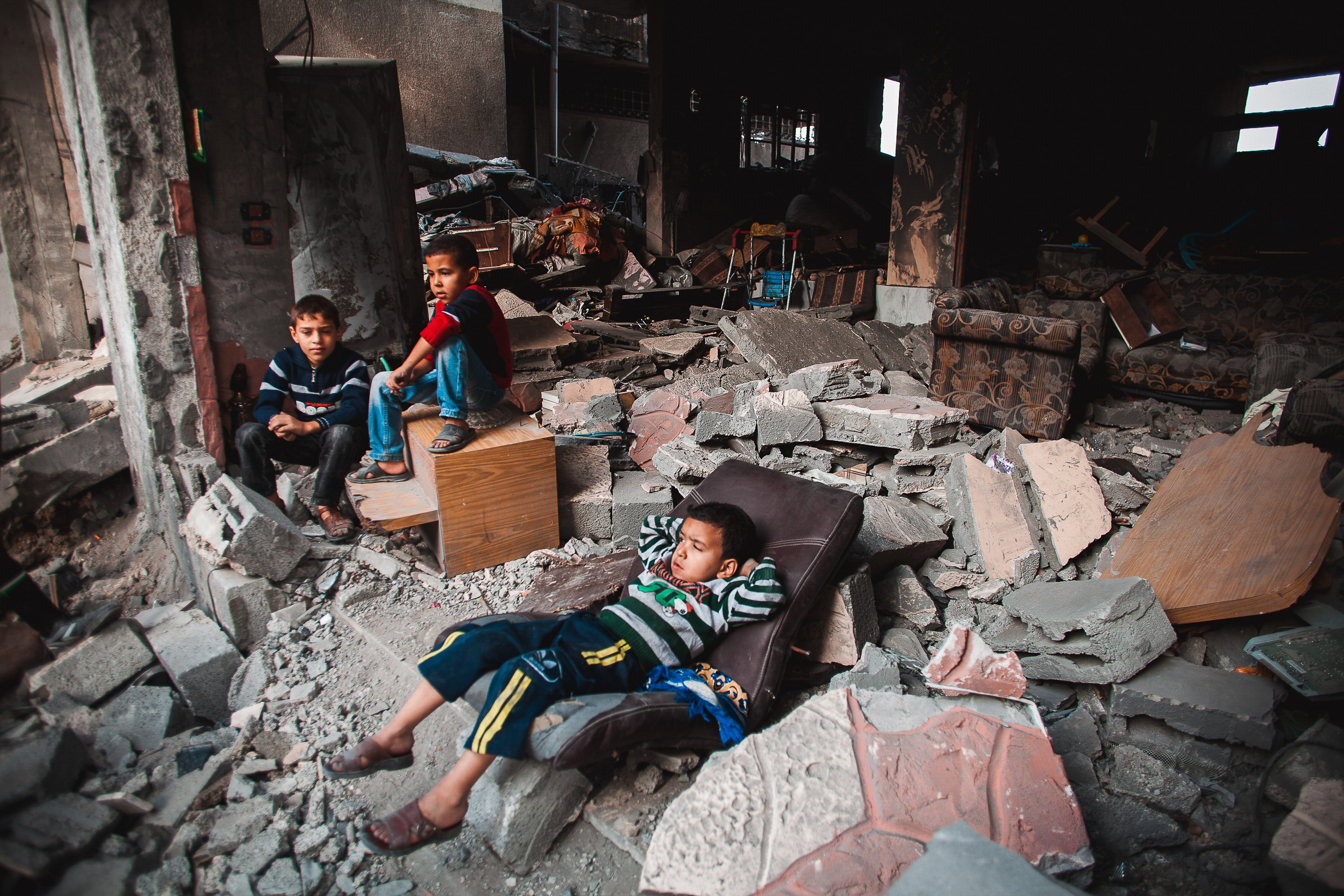 Baraa Azam is shown lying in front of his destroyed house after an Israeli airstrike flattened it at the Al Zaitoun area in Gaza City. Baraa was slightly injured during the air strike. His mother says he keeps asking, "How will the bus of school manage to pick me up with all the rubble around?"