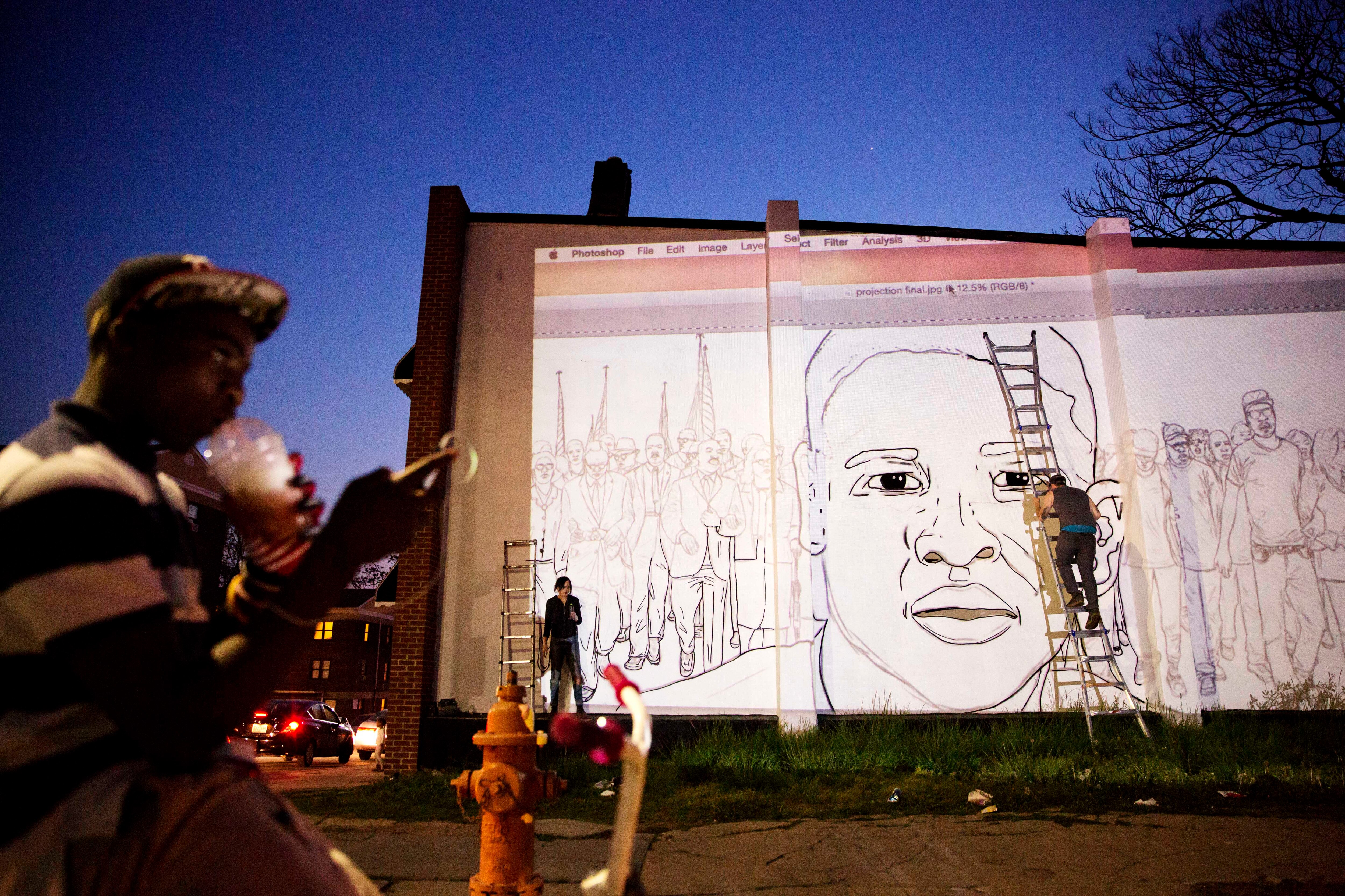 A mural of Freddie Gray is painted on the side of a building by local artist Nether, right, across the street from a makeshift memorial where Gray was arrested Sunday, May 3, 2015, in Baltimore. Baltimore's mayor has lifted a citywide curfew six days after riots were sparked over the death of a Gray who suffered a severe spinal injury while in police custody.