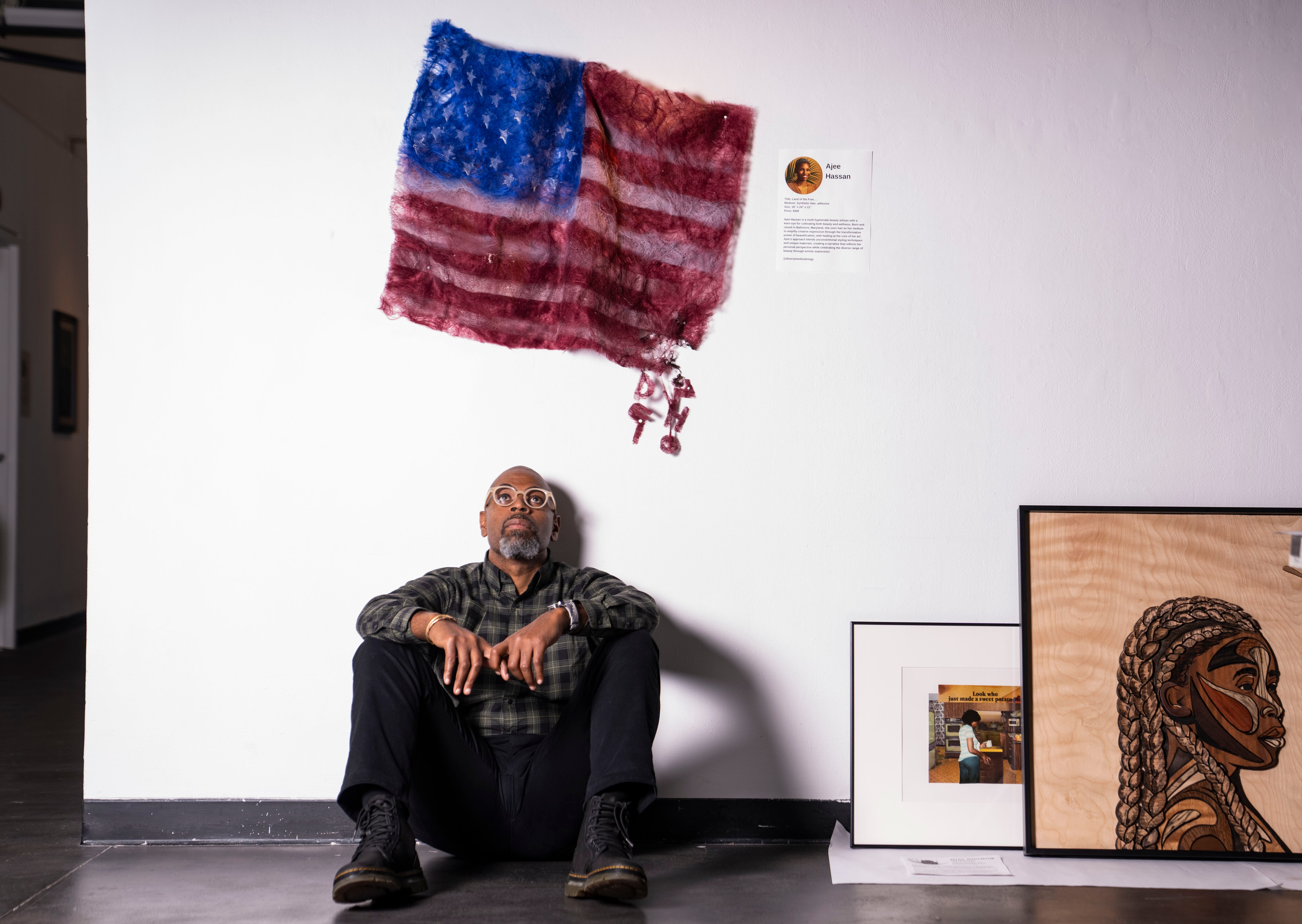 Jason Steer, Executive Director of Creative Alliance, sits in front of a piece titled “Land of the Free….” created by artist Ajee Hassan. 