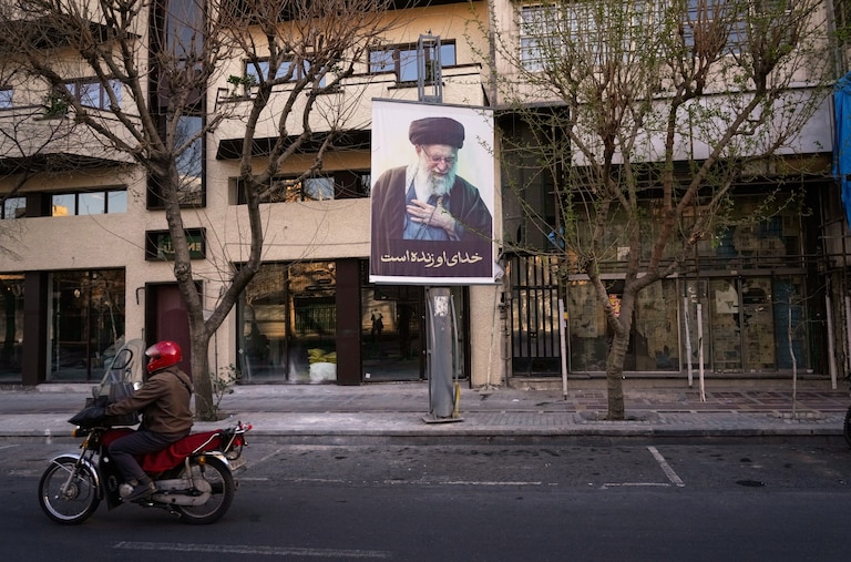 A motorcycle drives past a picture of the late Iranian Supreme Leader Ayatollah Ali Khamenei along an empty street in Tehran, Iran, Sunday, March 1, 2026, following the confirmed death of Khamenei in U.S. and Israeli strikes.