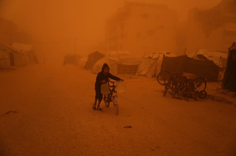 A boy pushes a bicycle carrying jerrycans of water through a sandstorm in Khan Younis, southern Gaza Strip, Saturday, March 14, 2026.