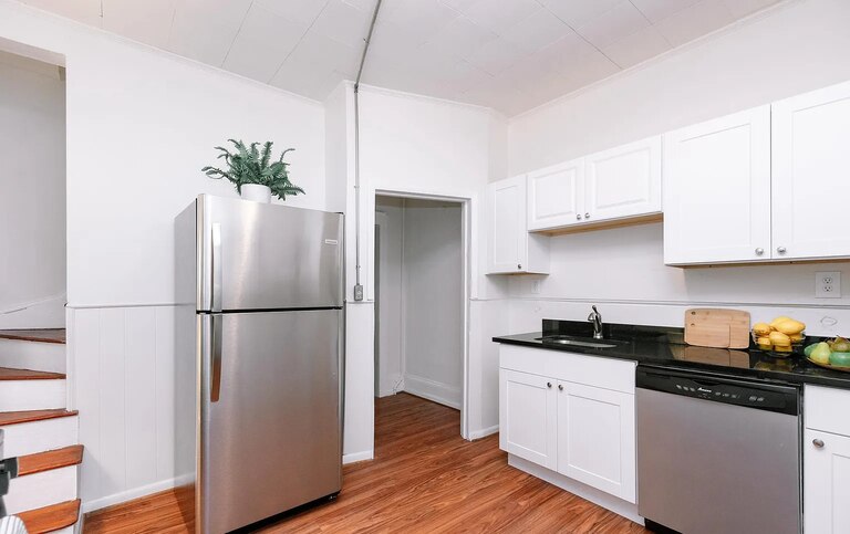 Bright kitchen with white cabinets, black countertops and stainless steel appliances.