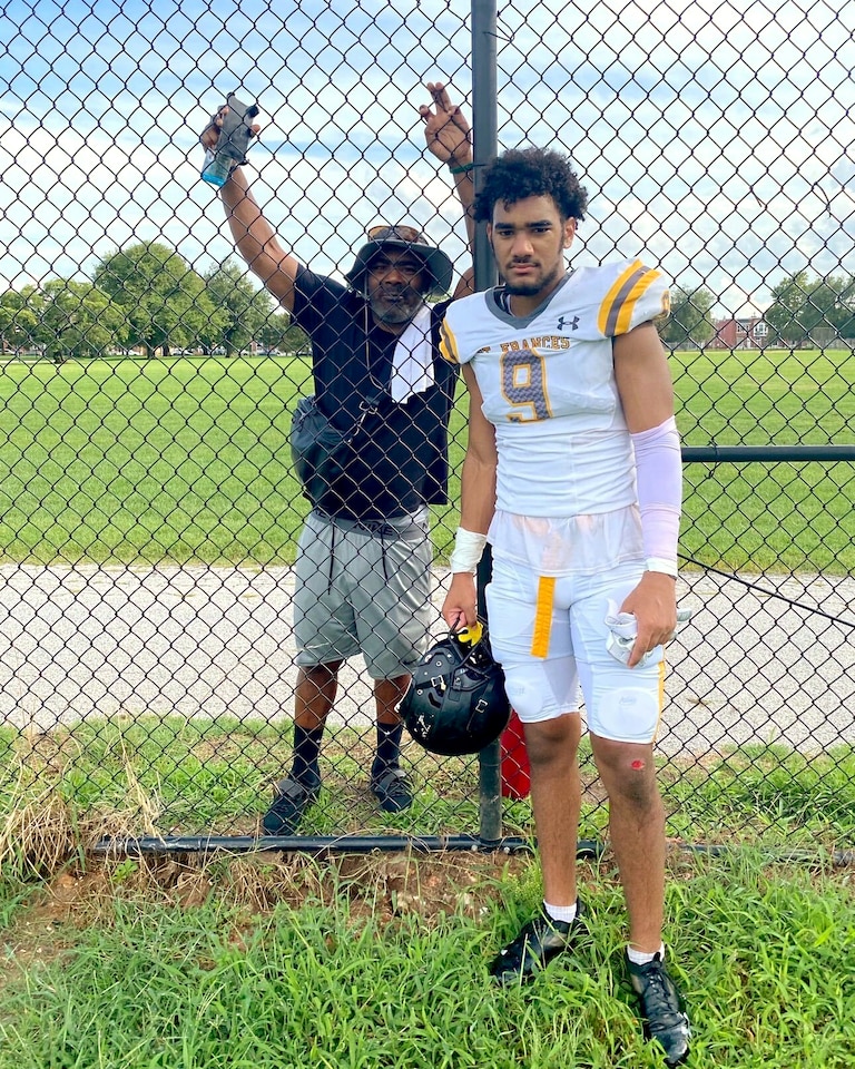 Elijah Sarratt poses with his father Donnie Sarratt, outside a fence during a team practice. The Sarratt family hails from Stafford, Va., but lost their family home in a 2021 fire.