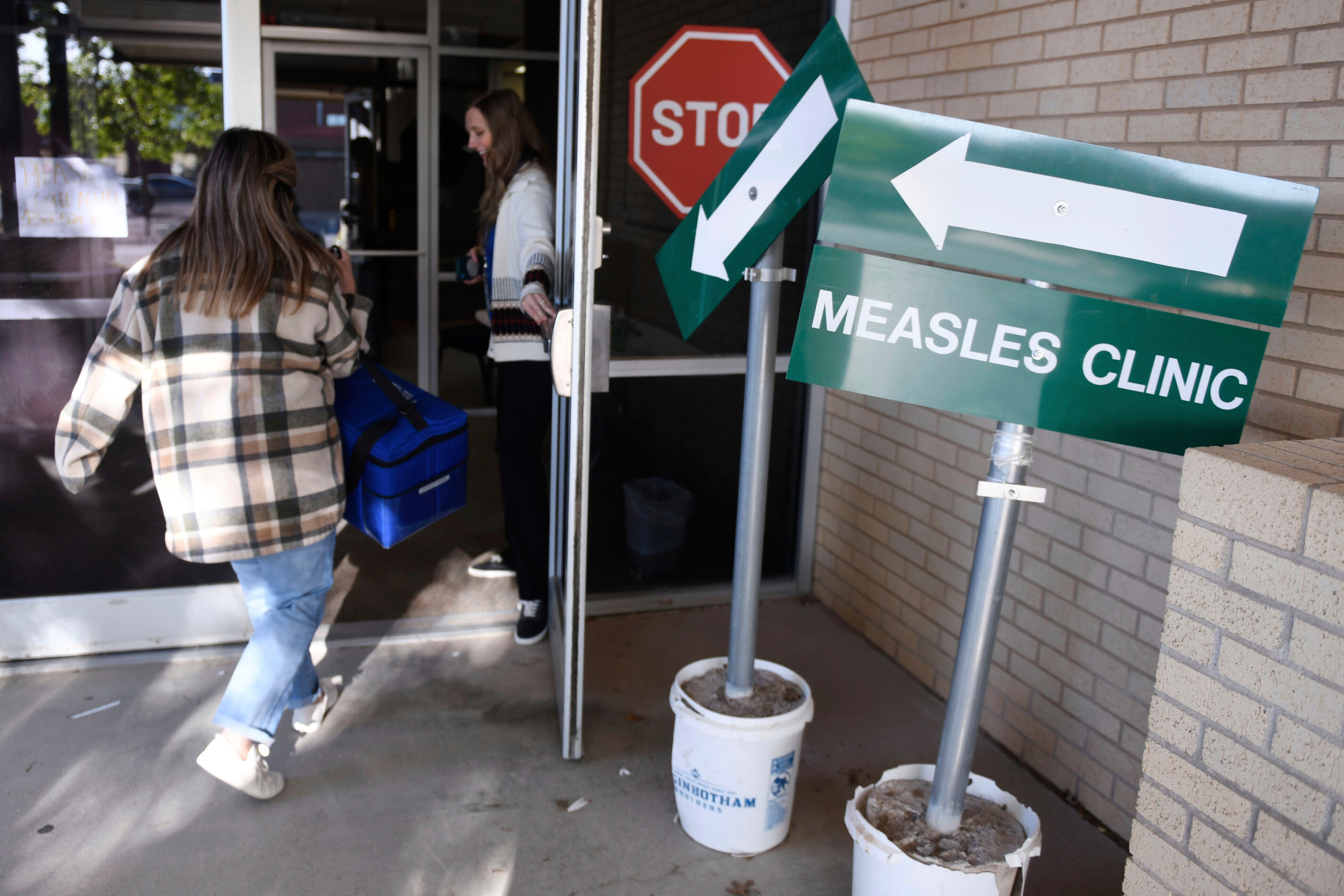 FILE - Health department staff members enter the Andrews County Health Department measles clinic carrying doses of the measles, mumps and rubella vaccine, April 8, 2025, in Andrews, Texas. (AP Photo/Annie Rice, File)