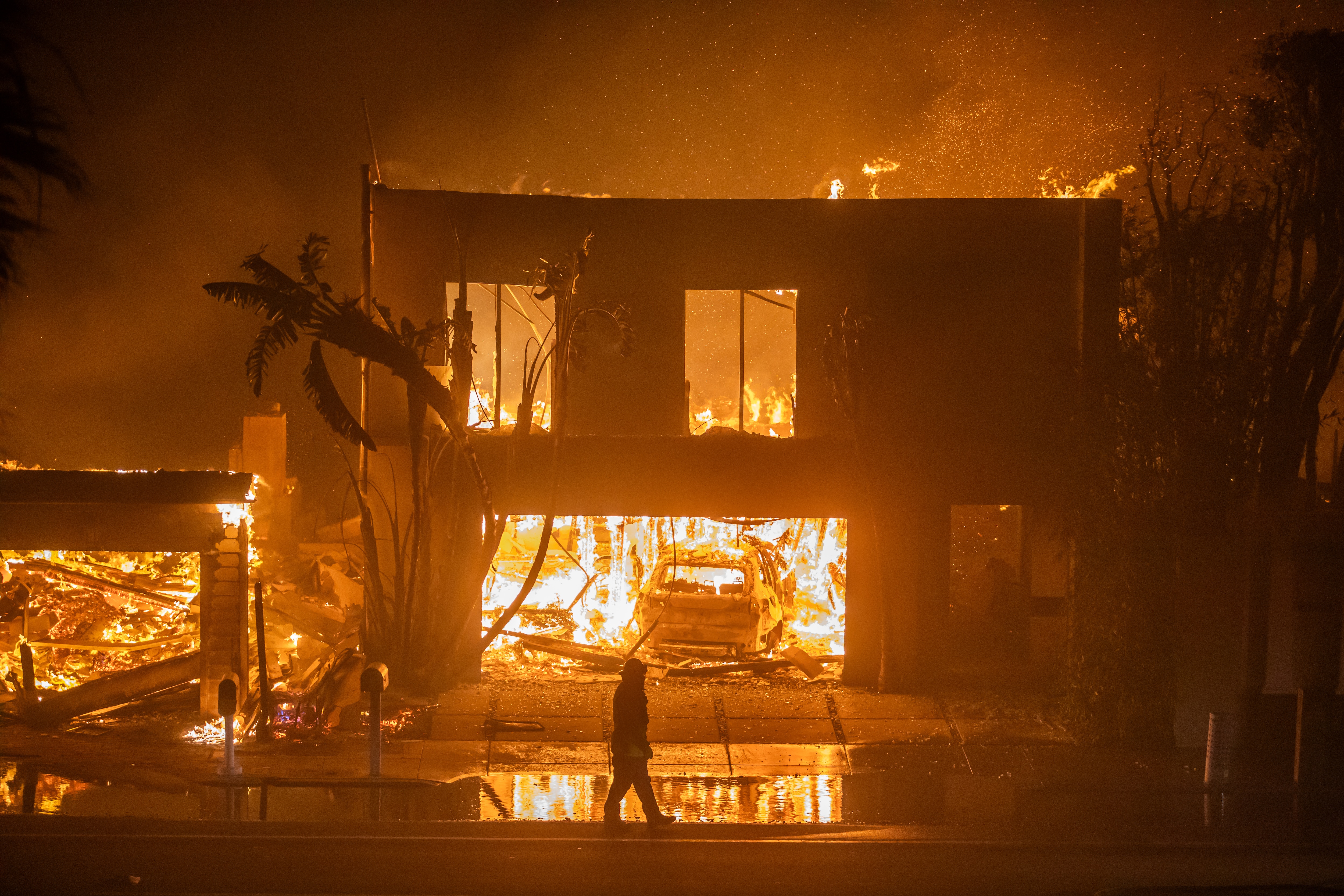 LOS ANGELES, CALIFORNIA - JANUARY 8: A firefighter watches the flames from the Palisades Fire burning homes on the Pacific Coast Highway amid a powerful windstorm on January 8, 2025 in Los Angeles, California.  The fast-moving wildfire has grown to more than 2900-acres and is threatening homes in the coastal neighborhood amid intense Santa Ana Winds and dry conditions in Southern California.