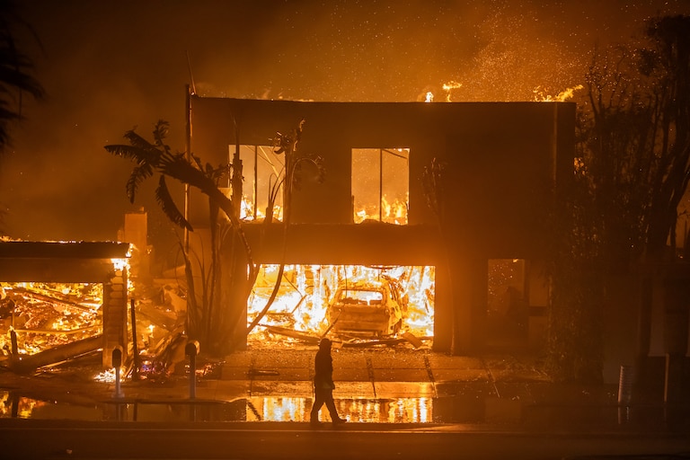LOS ANGELES, CALIFORNIA - JANUARY 8: A firefighter watches the flames from the Palisades Fire burning homes on the Pacific Coast Highway amid a powerful windstorm on January 8, 2025 in Los Angeles, California. The fast-moving wildfire has grown to more than 2900-acres and is threatening homes in the coastal neighborhood amid intense Santa Ana Winds and dry conditions in Southern California.