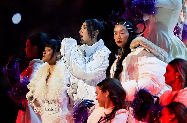 KPop Demon Hunters' Singers EJAE, Audrey Nuna, and Rei Ami in white coats performing at the halftime show of the Minnesota Vikings and Detroit Lions game on Christmas Day 2025.