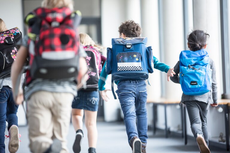 Rear view of pupils rushing down school corridor.